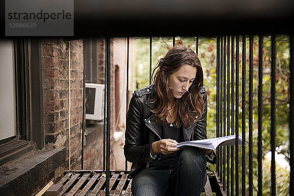 Seriöse Frau liest Buch  während sie an der Feuertreppe sitzt