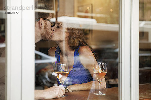 Zärtliches Paar küsst sich im Restaurant durch ein Fenster gesehen