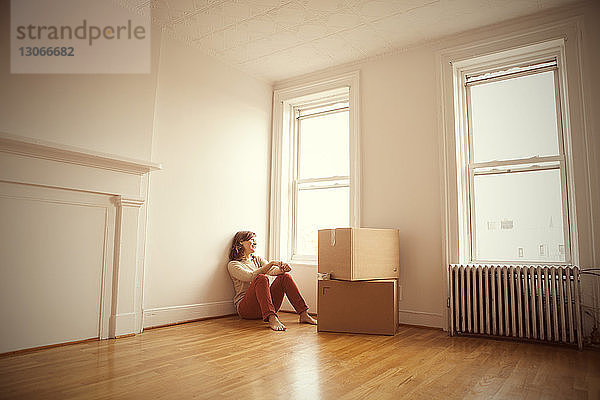 Frau schaut weg  während sie im neuen Haus auf dem Boden sitzt