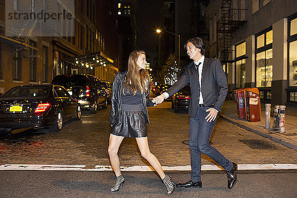 Fröhliches Paar  das sich an den Händen hält und nachts auf der Straße der Stadt spazieren geht