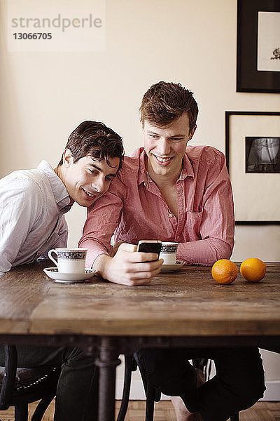 Schwules Paar benutzt Smartphone  während es zu Hause am Tisch sitzt