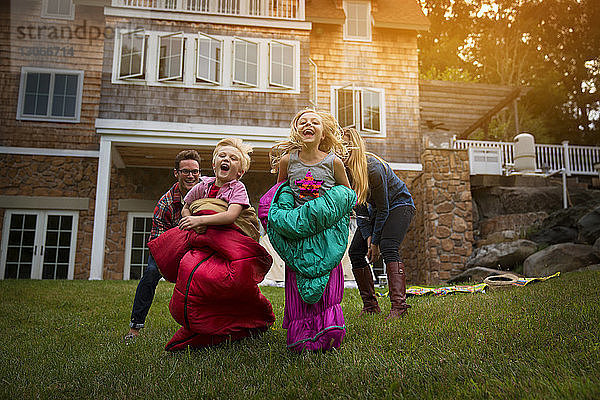 Eltern rennen hinter fröhlichen Kindern im Schlafsack gegen Haus im Hof