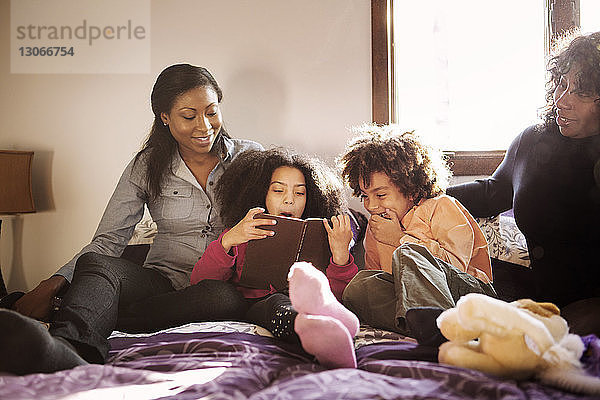 Glückliche Familie liest zu Hause auf dem Bett sitzend ein Buch