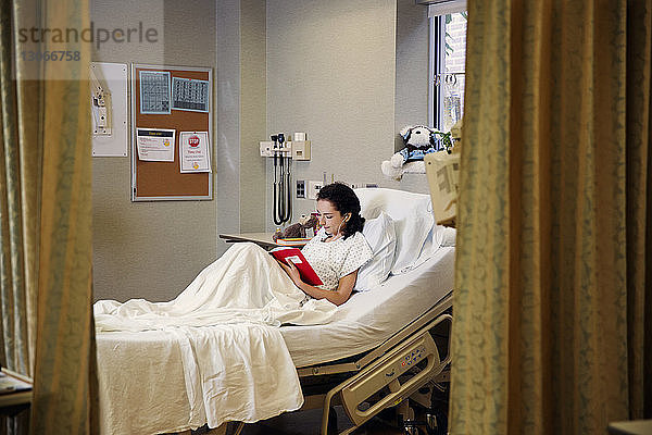 Patienten lesen Buch  während sie auf der Krankenstation im Bett sitzen