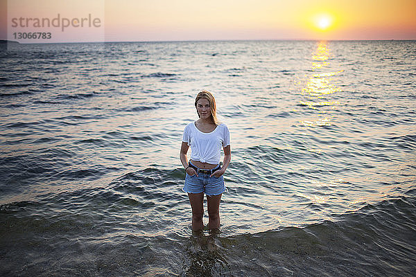 Bildnis einer Frau mit Händen in Taschen  die am Strand im Wasser steht