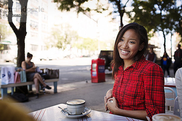 Lächelnde Frau schaut Freunde an  während sie im Straßencafé sitzt