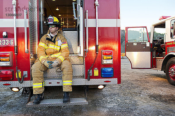 Feuerwehrmann schaut weg  während er auf den Stufen eines Feuerwehrwagens sitzt