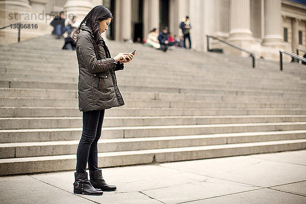Frau benutzt Mobiltelefon  während sie am Fussweg steht