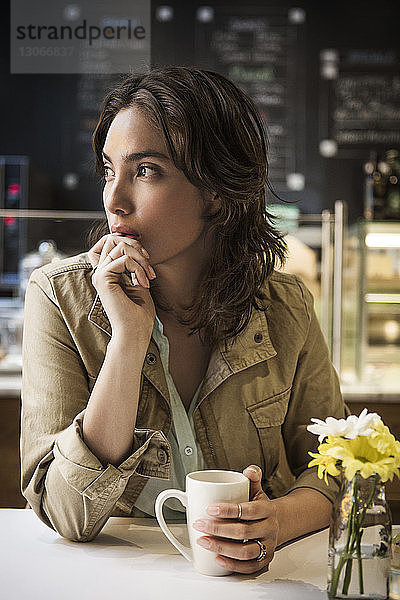Nachdenkliche Frau mit Kaffeetasse sitzt am Tisch im Café