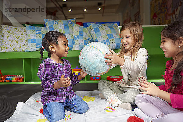 Glückliche Mädchen spielen mit Globus auf Decke bei der Kinderbetreuung