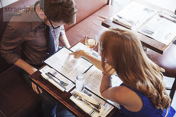 Frau zeigt mit dem Finger auf die Speisekarte  während sie mit ihrem Freund im Restaurant sitzt
