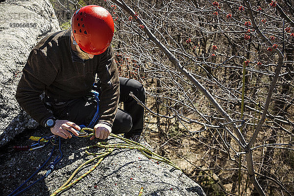 Hochwinkelansicht eines Mannes  der Karabiner mit einem Seil bindet  während er auf einer Klippe sitzt