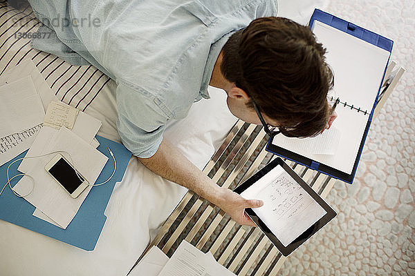 Draufsicht eines Mannes  der einen Tablet-Computer benutzt  während er zu Hause am Bett arbeitet