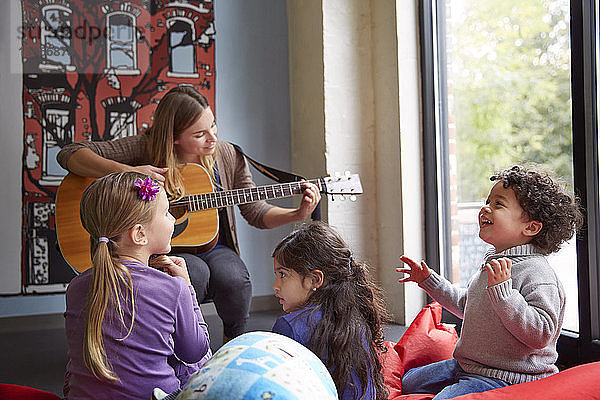 Lehrerin spielt Gitarre  während sich Kinder in der Vorschule vergnügen