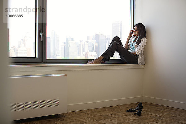 Geschäftsfrau benutzt Mobiltelefon  während sie auf dem Fensterbrett sitzt