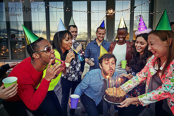 Mann bläst Kerzen auf einer Geburtstagstorte aus  die von einer Frau gehalten wird  während sie mit Freunden auf einer Party genießt