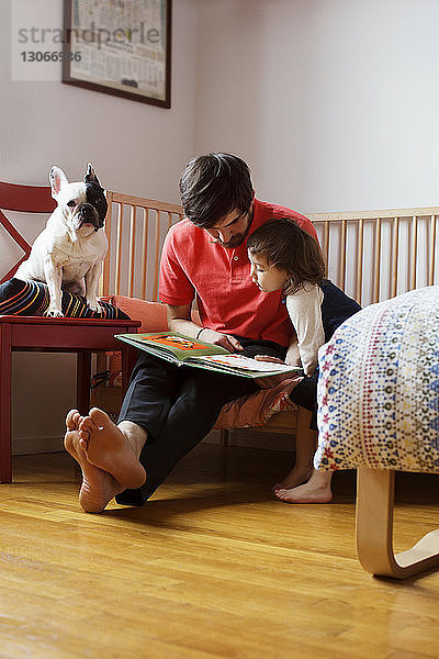 Vater und Tochter schauen sich ein Buch an  während sie mit dem Hund zu Hause sitzen