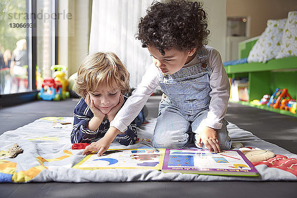 Freunde lesen Bilderbuch  während sie sich in der Kinderbetreuung auf einer Decke ausruhen