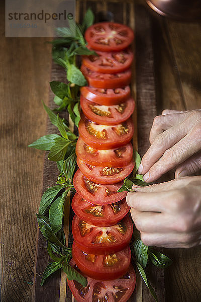 Ausgeschnittenes Bild einer Frau  die bei Tisch Minzblätter in Tomatensalat anordnet