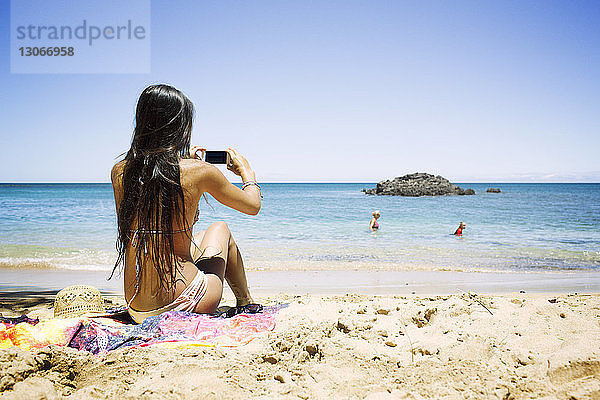 Rückansicht einer Frau  die am Strand fotografiert