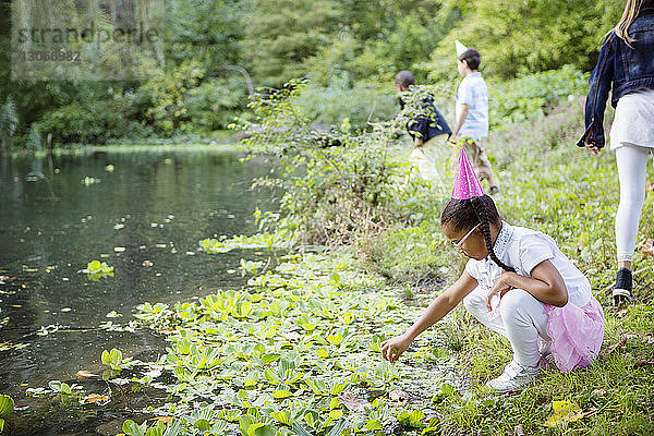 Mädchen schaut sich Pflanzen an  während Freunde am See spielen
