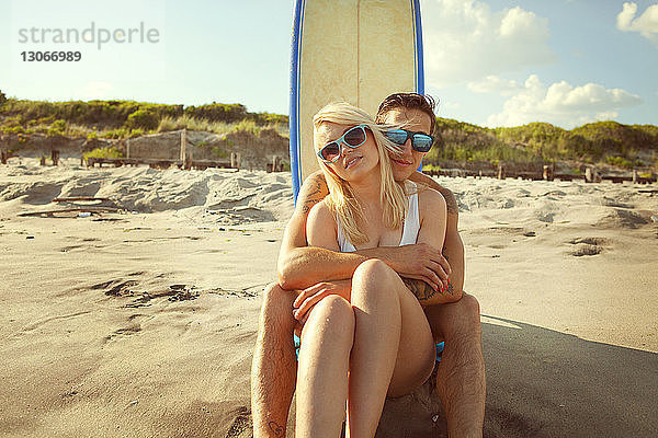 Porträt eines romantischen Paares am Strand  das am Surfbrett sitzt