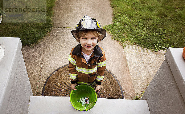 Porträt eines Jungen im Feuerwehrkostüm  der während eines Streichens oder Behandelns an der Tür steht