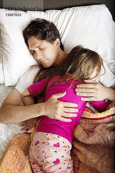Draufsicht auf den Vater  der mit der Tochter zu Hause im Bett schläft