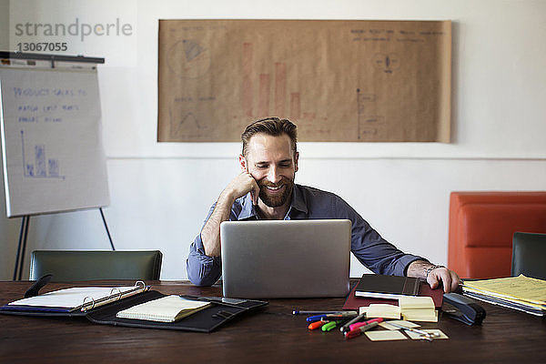 Lächelnder Geschäftsmann schaut auf Laptop-Computer  während er im Büro sitzt