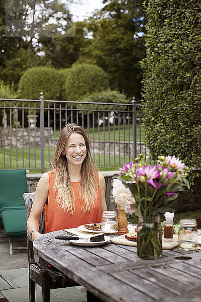 Glückliche Frau sitzt am Frühstückstisch auf dem Rasen