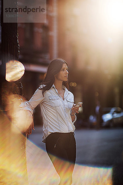 Frau schaut weg  während sie ein Smartphone an der Straße hält