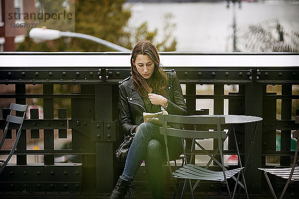 Frau liest Buch  während sie am Tisch auf einer Brücke in der Stadt sitzt