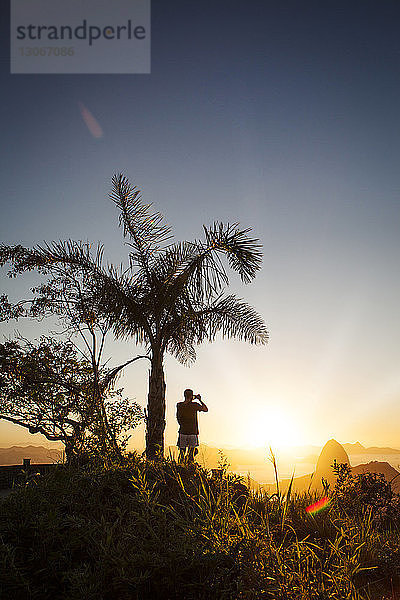 Rückansicht eines Mannes  der den Zuckerhut bei Sonnenuntergang fotografiert
