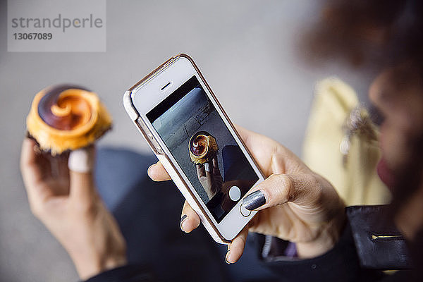 Ausgeschnittenes Bild einer Frau  die mit einem Smartphone Muffin fotografiert