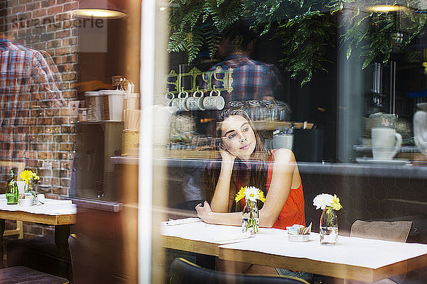 Nachdenkliche Frau sitzt im Restaurant durch Glasfenster gesehen