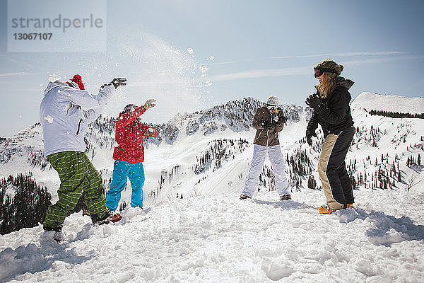 Glückliche Skifahrer spielen mit Schnee  während sie auf einem schneebedeckten Feld stehen