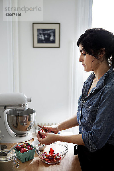 Frau schneidet Erdbeeren  während sie zu Hause in der Küche steht