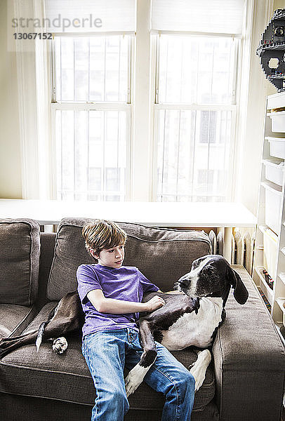 Junge mit Hund entspannt sich zu Hause auf dem Sofa