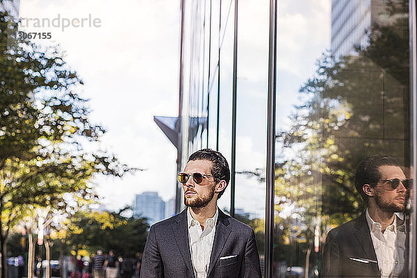 Geschäftsmann trägt Sonnenbrille  die auf Glasgebäude in der Stadt reflektiert