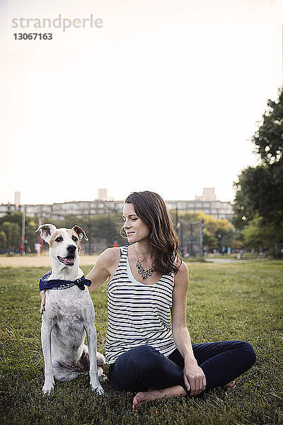 Frau sitzt mit Hund auf Grasfeld vor klarem Himmel im Park