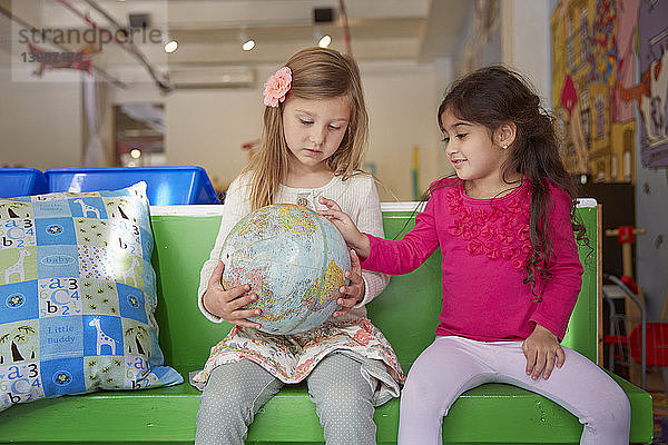 Mädchen betrachten den Globus  während sie in der Kinderbetreuung auf dem grünen Sitz sitzen