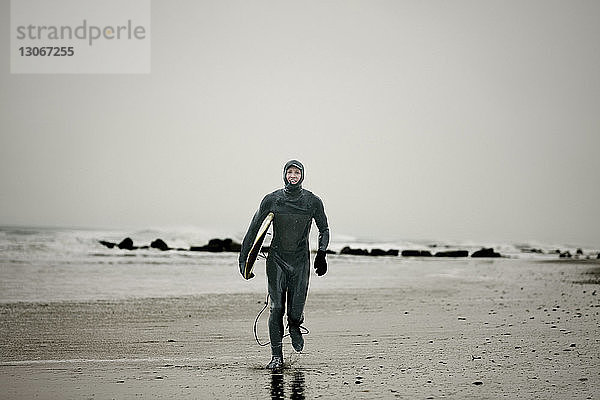 Porträt eines Mannes im Taucheranzug beim Spaziergang am Strand vor klarem Himmel