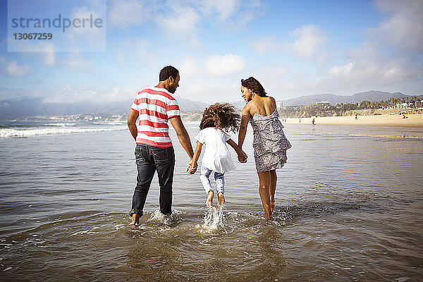 Mädchen springt beim Spaziergang mit den Eltern am Strand im Wasser
