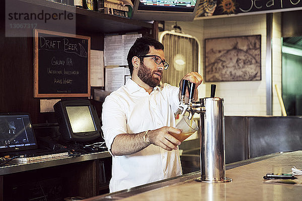 Mann gießt Bier aus dem Zapfhahn  während er im Restaurant steht