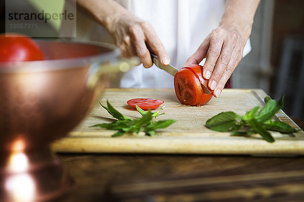 Mitschnitt einer Frau  die auf einem Schneidebrett Tomatenscheiben nach Minzblättern schneidet