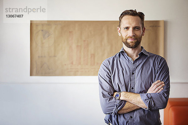 Porträt eines Geschäftsmannes mit verschränkten Armen  der im Büro an der Wand steht