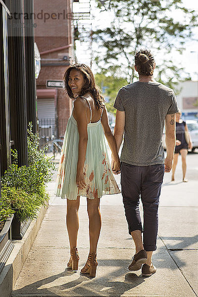 Rückansicht eines Paares  das an einem sonnigen Tag auf dem Bürgersteig geht