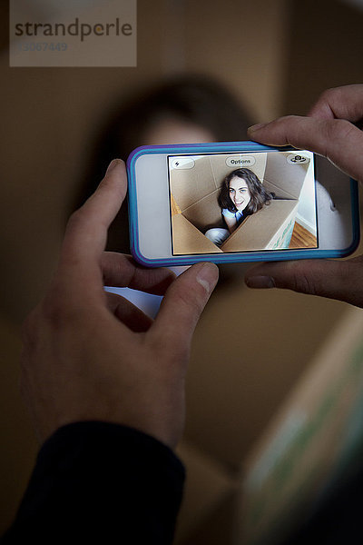 Ausschnitt eines Mannes  der eine Frau fotografiert  die zu Hause in einem Pappkarton sitzt