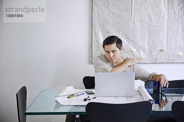 Müder Mann hält Schulter bei der Arbeit am Laptop im Büro