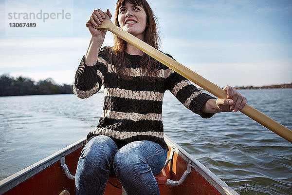 Lächelnde Frau rudert im Winter auf dem See gegen den Himmel